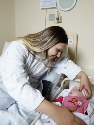 Mulher loira em quarto de hospital faz carinho em um bebê com síndrome de Down. Crédito da foto: Isaías Emilio da Silva