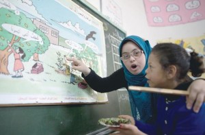 Hiba Al Sharfa, a primeira professora com síndrome de Down da Faixa de Gaza, aparece ensinando uma criança com síndrome de Down. Enquanto a aluna olha para um mapa exposto no quadro negro, a professora aponta para o mesmo mapa e fala algo sobre o tema.