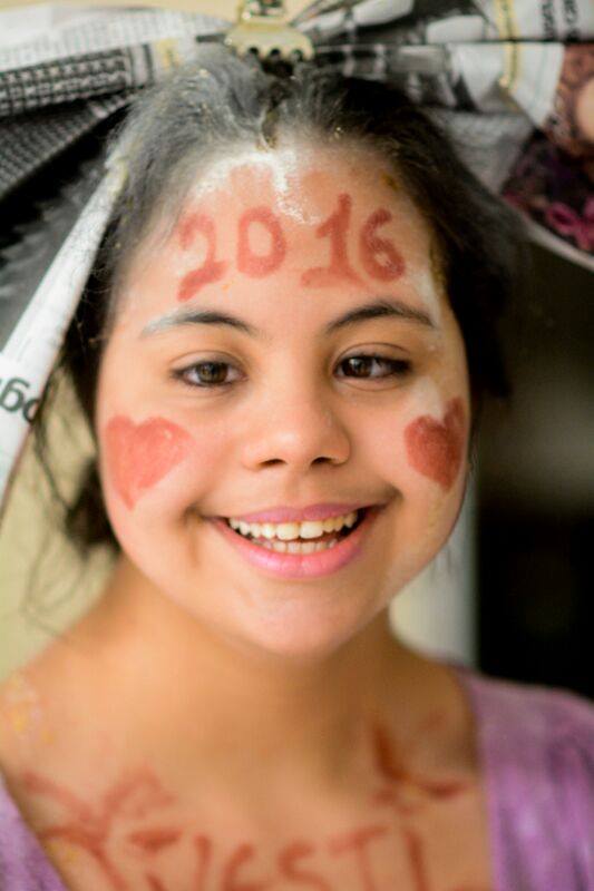 Marina, com o rosto pintado de vermelho, um coracao e o ano 2016 e um lacarote de jornal na cabeca.