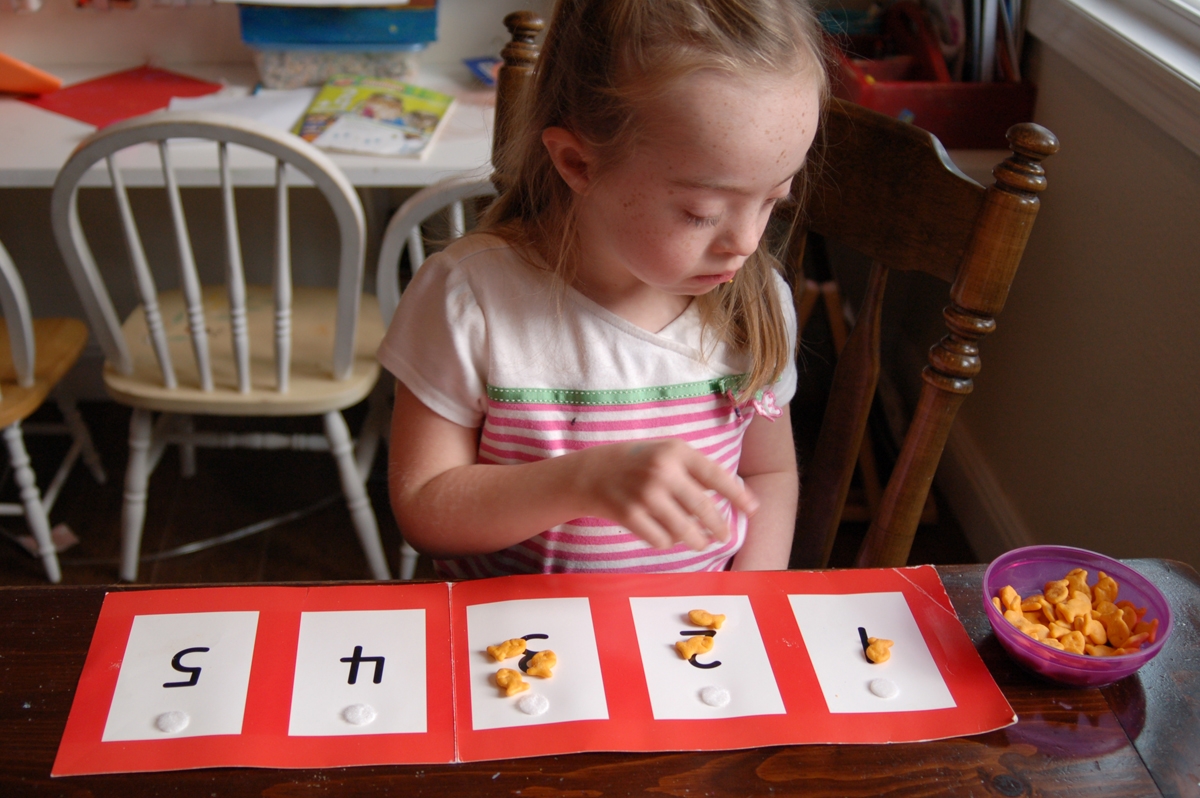 menina com sindrome de Down colocando biscoitos em cima de numeros escritos em cartolina